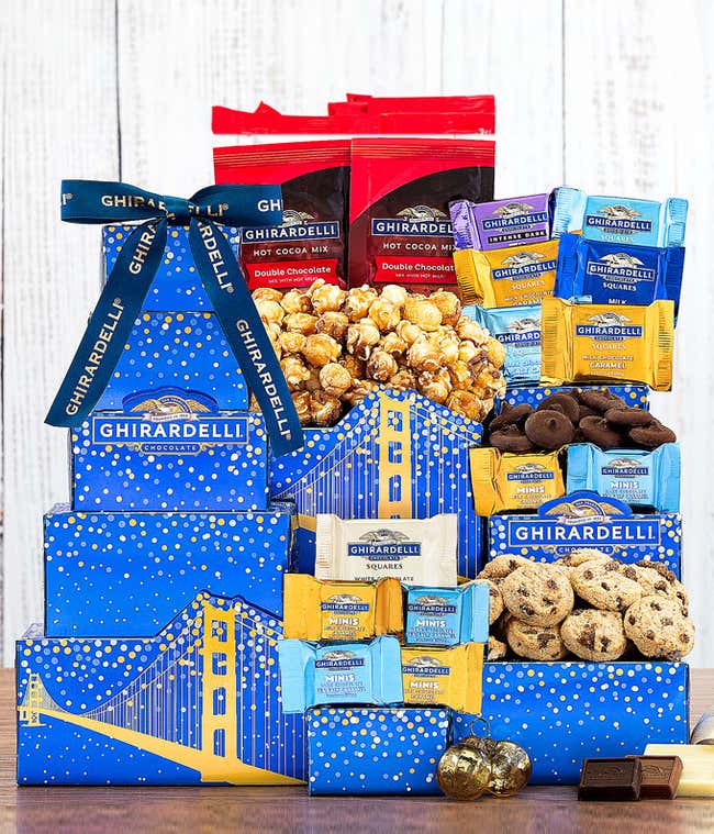 Ghirardelli-themed gift tower with blue boxes featuring golden bridge designs. Contains an assortment of Ghirardelli chocolates, including squares, minis, hot cocoa mix, caramel popcorn, cookies, and chocolate-covered almonds, tied with a Ghirardelli ribb